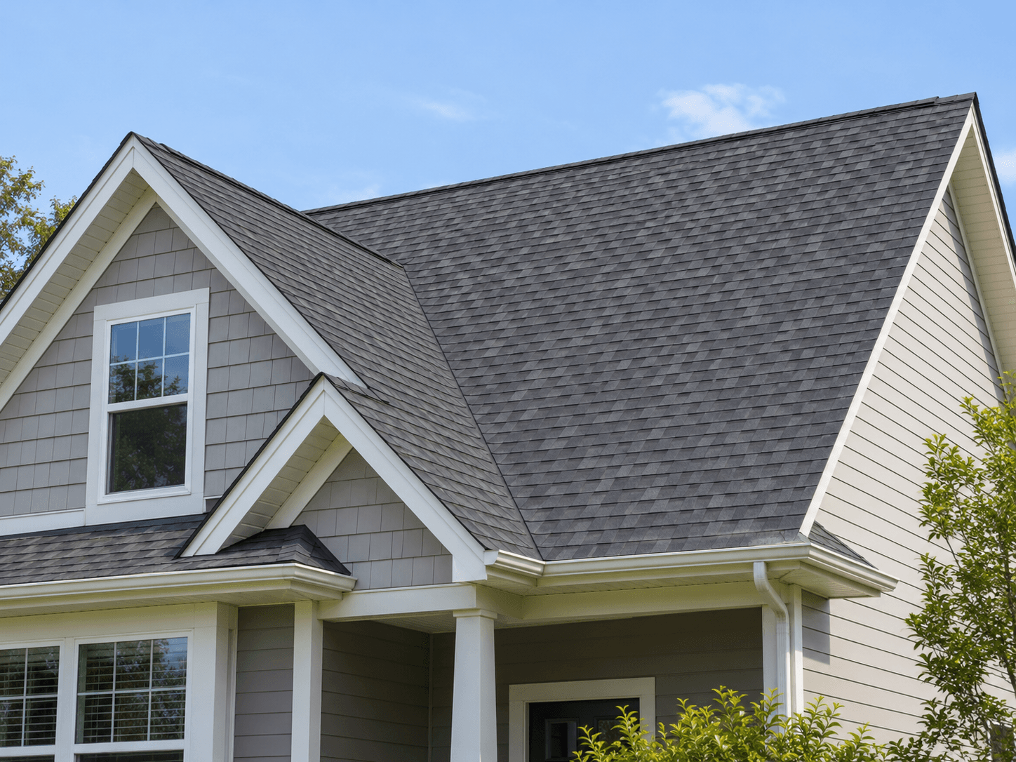 A shingle roof with gables and gutters on a gray-sided house.